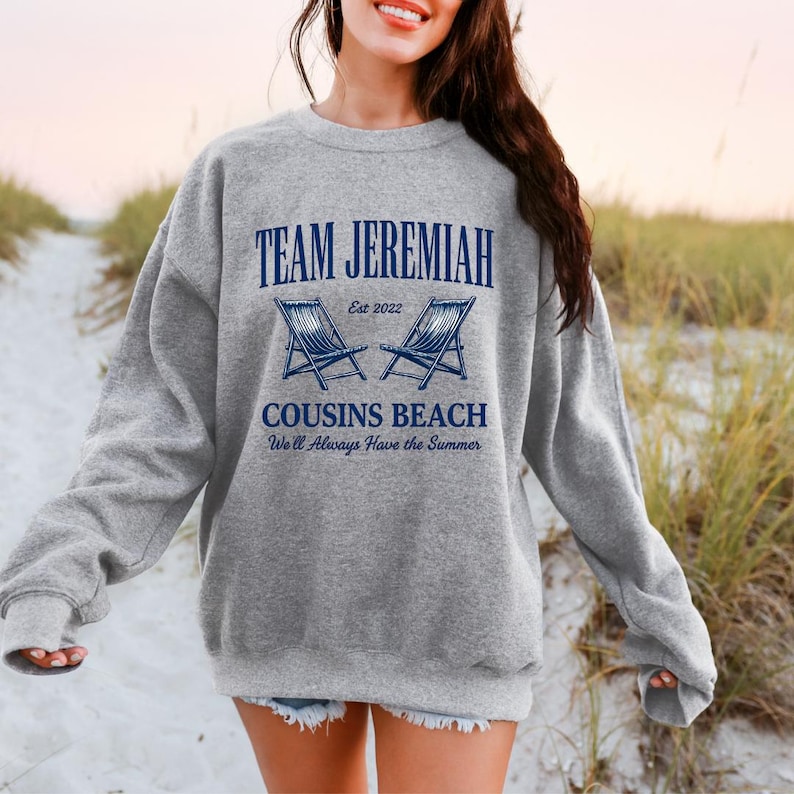 May include: A gray sweatshirt with the text "TEAM JEREMIAH" above two blue beach chairs and the words "COUSINS BEACH" and "We'll Always Have the Summer". The sweatshirt is a crew neck style.