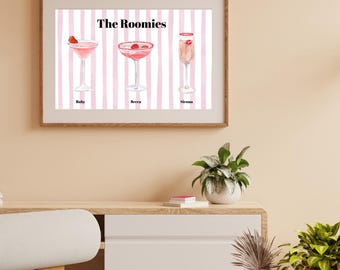 May include: A framed print featuring three cocktail illustrations: Ruby, Becca, and Sienna. The cocktails are pink and garnished with fruit, set against a pink and white striped background. The title "The Roomies" is at the top.