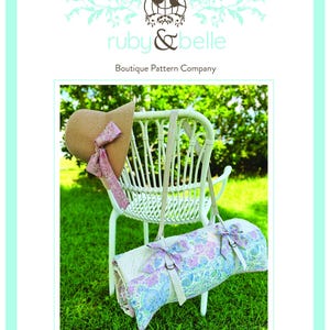 Könnte beinhalten: Weißer Korbstuhl mit Strohhut und Picknickrolle. Der Hut hat ein rosa Band. Die Picknickrolle ist aufgerollt und hat ein Blumenmuster mit rosa und blauen Akzenten. Der Text "Sophie Picnic Roll Up" steht unten.