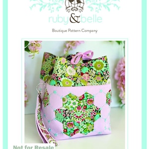 May include: A Charlotte Bag pattern by Ruby & Belle. The bag has a floral print top and a light pink body with a floral star design. It includes a matching strap and a pink bow. The text "Not for Resale" is visible.