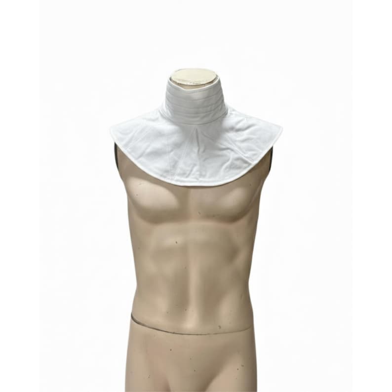 May include: A white, high-collared garment, possibly a neck ruff or accessory, is displayed on a mannequin. The collar has a pleated design and a wide, rounded shape. The mannequin is a neutral skin tone, set against a plain white background.