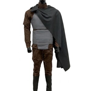 Pode incluir: Um traje completo em tons de castanho e cinza. O traje inclui um casaco castanho com costuras bege, uma armadura peitoral cinzenta, cal&ccedil;as castanhas e botas pretas. Uma capa cinzenta escura cobre os ombros.