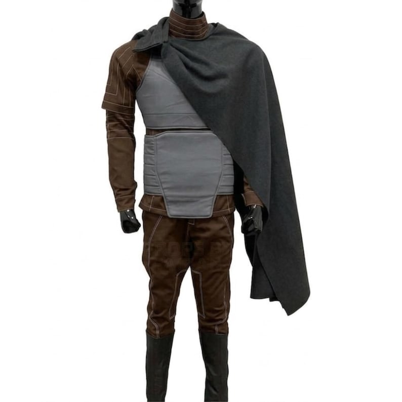 Pode incluir: Um traje completo em tons de castanho e cinza. O traje inclui um casaco castanho com costuras bege, uma armadura peitoral cinzenta, cal&ccedil;as castanhas e botas pretas. Uma capa cinzenta escura cobre os ombros.