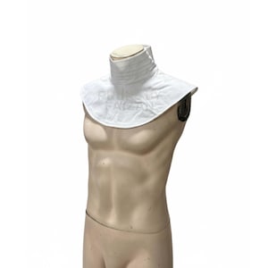 May include: A white, high-collared garment with a pleated neck and a wide, rounded collar. The garment is displayed on a mannequin, showcasing its shape and design. The fabric appears to be smooth and opaque.