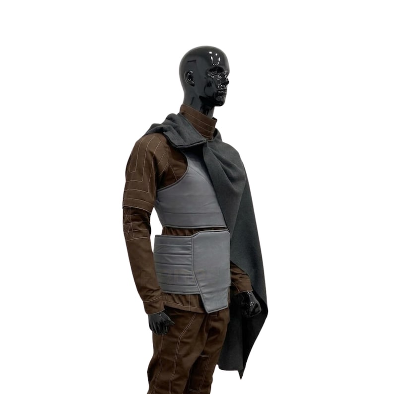 Pode incluir: Um traje marrom e cinza exibido em um manequim preto. O traje inclui uma jaqueta marrom, cal&ccedil;as e um colete cinza com cinto combinando. Uma capa cinza escuro &eacute; drapeada sobre os ombros.