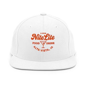 May include: White flat-brim baseball cap with the orange text "The Nite Lite FOOD DRINK ALTA VISTA, IA" and a martini glass graphic. The cap has a structured fit and a curved brim.
