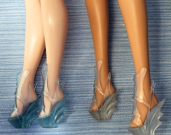 May include: Two pairs of high-heeled shoes with clear plastic uppers and blue iridescent accents. The shoes have a pointed toe and a high stiletto heel.