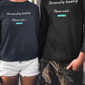 May include: Two long-sleeved sweatshirts, one navy blue and one black, each with the text "Personality loading Please wait..." above a loading bar graphic. The navy sweatshirt is paired with white shorts.