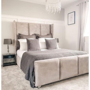 Könnte beinhalten: Ein luxuriöses Schlafzimmer mit einem großen Bett mit hohem, gepolstertem Kopfteil. Das Bett ist mit einer grauen Decke und Kissen bedeckt. Ein Kristall-Kronleuchter hängt von der Decke, und ein Nachttisch mit einer Lampe ist sichtbar.