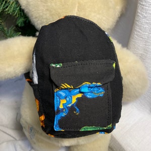 May include: A small black backpack with a dinosaur print. The backpack has a front pocket with a blue dinosaur on it.
