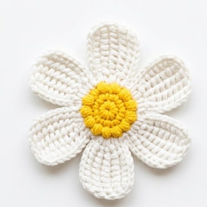May include: A handmade crochet daisy with six white petals surrounding a yellow center. The daisy is crafted with a textured stitch, creating a three-dimensional effect. The flower is likely used for decorative purposes or as an embellishment.