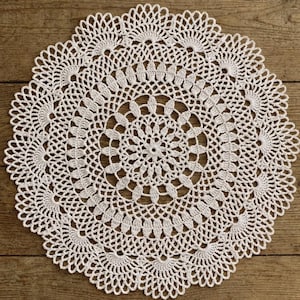 Peut inclure: Napperon rond blanc en crochet, avec un motif ajouré complexe. Le napperon présente un motif floral central entouré de plusieurs couches de dentelle détaillée. L'esthétique générale est délicate et faite à la main, adaptée à la décoration intérieure.