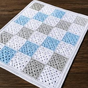 May include: A handmade crochet blanket with a diamond pattern in white, light blue, and gray squares. The blanket is made of soft yarn and has a white border. The blanket measures approximately 36 inches by 48 inches.