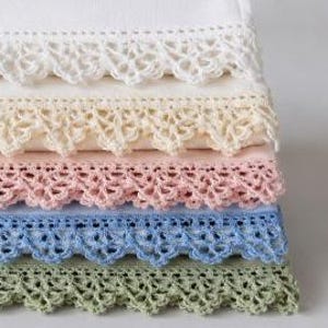 May include: A stack of folded linens in pastel shades, each with a delicate, crocheted lace trim. The colours include white, cream, pale pink, light blue, and green, creating a soft, inviting aesthetic.