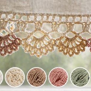 May include: A close-up of a crocheted valance with a scalloped edge in shades of cream, brown, and pink. Below the valance are six balls of yarn in coordinating colors. The valance is hanging in front of a window.