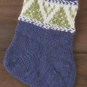 May include: A blue knitted Christmas stocking with a white cuff featuring green tree designs. The cuff is trimmed with a white and blue border. The stocking is made of a textured yarn.