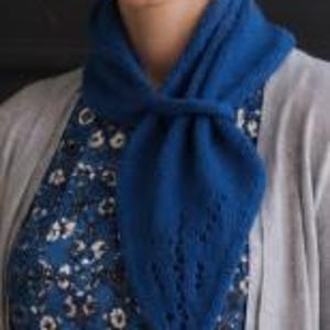 May include: A vibrant blue knitted scarf featuring a triangular shape and delicate eyelet lace detailing along the pointed end. The scarf is tied in a simple knot around the neck, layered over a blue floral patterned top and a light gray cardigan.
