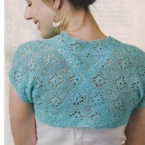 Peut inclure: Un boléro bleu clair à manches courtes présentant un motif complexe en crochet ajouré avec un dessin géométrique répétitif. Le vêtement possède une encolure arrondie et une silhouette courte qui s'arrête au-dessus de la taille.