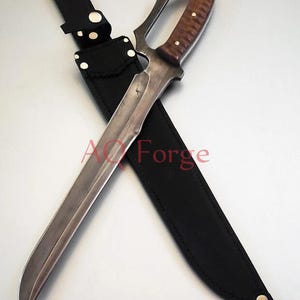 May include: A large, curved blade knife with a wooden handle and a black leather sheath. The knife has a silver blade and a dark brown handle. The sheath is black and has a strap with snaps. The text "AQ Forge" is visible.