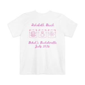 May include: A white short-sleeve t-shirt featuring pink text and line art graphics. The design includes the text Rehoboth Beach, Bekah's Bachelorette, July 2026, and three square frames containing a seashell, a diamond ring, and a sun icon.