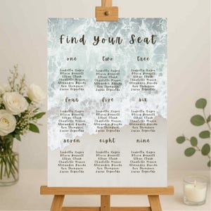 May include: A wedding seating plan with the words "Find Your Seat" in script. The background has a watercolour ocean wave design in blue and grey. Names are listed under numbers one to nine.