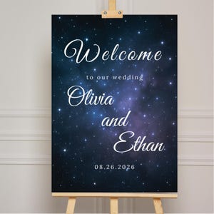 May include: A wedding welcome sign on an easel. The sign features a dark blue and purple galaxy background with white text that reads "Welcome to our wedding Olivia and Ethan 08.26.2026."
