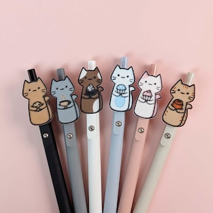 May include: Six colorful pens with cat-shaped toppers, each holding a different item. The pens have black, gray, white, blue, pink, and light gray barrels. The background is a solid light pink.