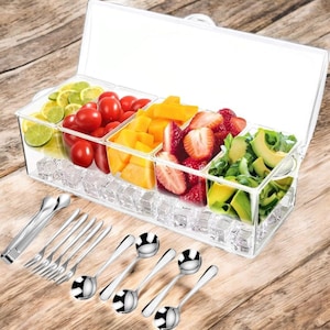 May include: A clear, divided serving container filled with ice and fresh fruit, including limes, tomatoes, mango, strawberries, and avocado. Stainless steel serving utensils, including tongs, forks, and spoons, are arranged on a wooden surface.
