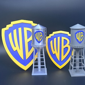 Puede incluir: Una exhibición con dos modelos de torres de agua grises y dos grandes logotipos en forma de escudo. Los logotipos son azules con ribete amarillo y las letras "WB" en amarillo. Las torres de agua tienen el logotipo "WB" en azul y amarillo.