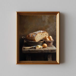 Puede incluir: Pintura enmarcada de naturaleza muerta con una hogaza de pan, huevos en una cesta y mantequilla sobre una mesa de madera. Un cuchillo descansa junto a la mantequilla. La pintura tiene una paleta de colores cálidos y una estética rústica.
