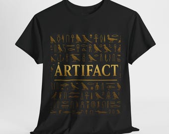 Puede incluir: Camiseta negra con un diseño dorado que presenta jeroglíficos egipcios y la palabra "ARTIFACT" en negrita dorada. El diseño incluye varios símbolos y figuras, creando una estética histórica y artística.