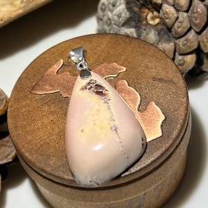 May include: A teardrop-shaped pendant with a light pink, yellow, and brown agate stone. The pendant is set in sterling silver and has a bail for attaching a chain.