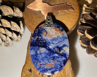 May include: A blue and copper oval pendant with a silver bail. The pendant is made of a natural stone with a swirling pattern.