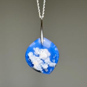 May include: A blue and white pendant necklace with a silver chain. The pendant has a unique shape and features a blue background with white cloud-like patterns. The necklace is a piece of jewelry.
