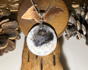 May include: A silver chain necklace with a round, white and gray agate pendant. The pendant has a silver bail and is set on a wooden surface.
