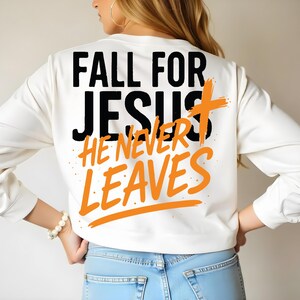 Back view of a white sweatshirt worn by a woman with long blonde hair. The design “Fall for Jesus, He Never Leaves” is prominently printed across the back in bold black and orange text, creating a powerful visual statement.
