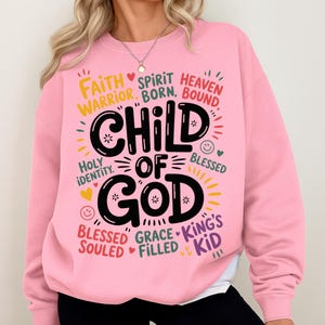 Woman wearing a light pink sweatshirt with the “Child of God” design prominently on the chest, surrounded by playful and encouraging spiritual words.