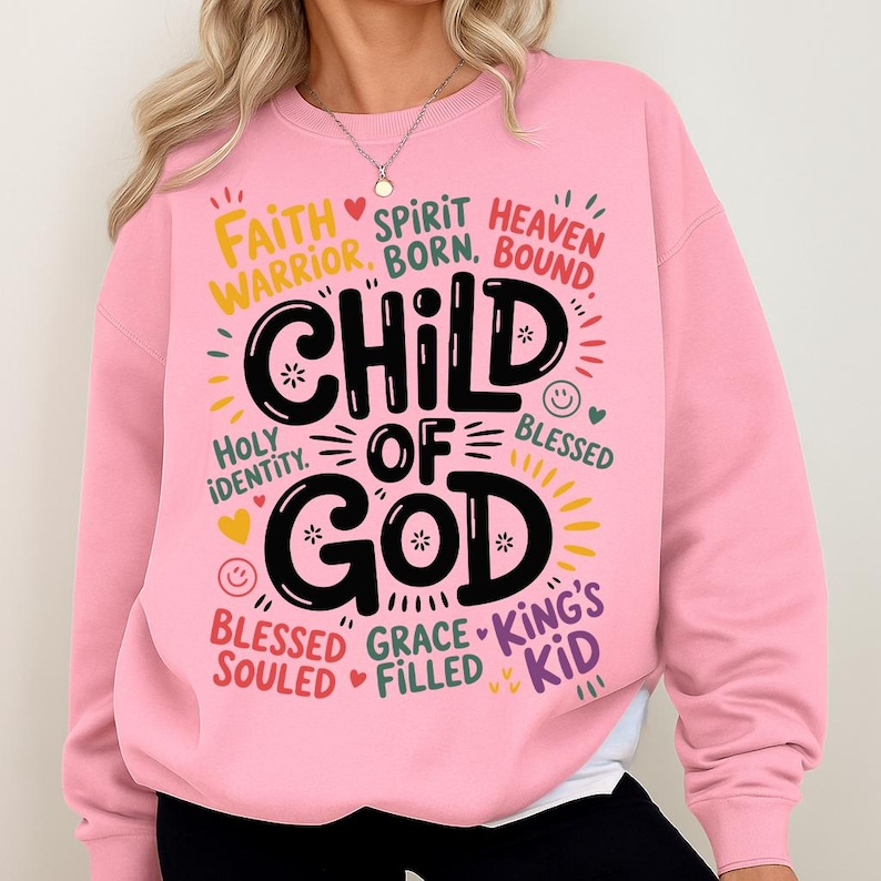 Woman wearing a light pink sweatshirt with the “Child of God” design prominently on the chest, surrounded by playful and encouraging spiritual words.