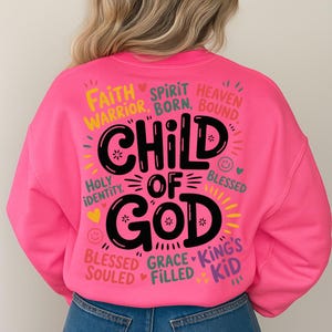 Back view of a woman in a bright pink sweatshirt showcasing the bold “Child of God” design filled with spiritual affirmations and cheerful decorative elements.