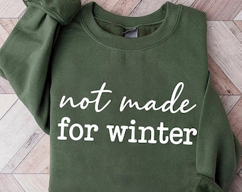 Puede incluir: Una sudadera verde oliva con el texto blanco "not made for winter". La parte superior de manga larga tiene cuello redondo y puños acanalados. La sudadera está hecha de un material suave.