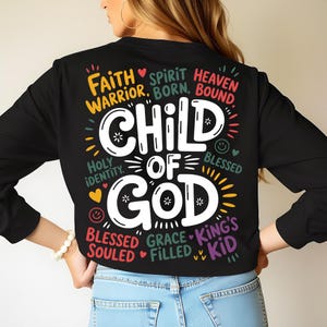 A woman shown from the back wearing a black sweatshirt with the “Child of God” design highlighted in the center, encircled by colorful spiritual phrases.