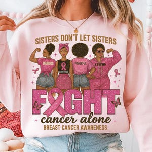 以下が含まれることがあります： 「Sisters Don't Let Sisters Fight Cancer Alone」の文字と4人の女性のグラフィックが描かれたピンク色のスウェットシャツ。各女性は異なる服装をしており、シャツにはWarrior、Survivor、Powerful、Strongの文字が書かれています。乳がん啓発。