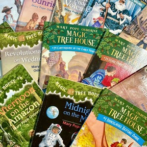 May include: A collection of children's books featuring colorful covers. Titles include "Magic Tree House" series books, such as "Dinosaurs Before Dark," "Midnight on the Moon," and "Earthquake in the Early Morning." The books are by Mary Pope Osborne.