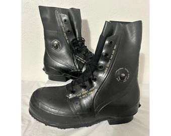 May include: A pair of black rubber military-style boots featuring black laces, metal eyelets, and a side air valve. The boots have printed text that reads "FOLD GUSSET THIS SIDE ONLY" and "KEEP DOUBLE LACED TO HOLD FIRMLY" along the side panels.
