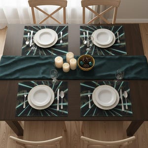 May include: A dining table set for four with white plates, cutlery, and placemats featuring a teal and gold design. A dark green runner, candles, and a bowl of pinecones complete the elegant setting.