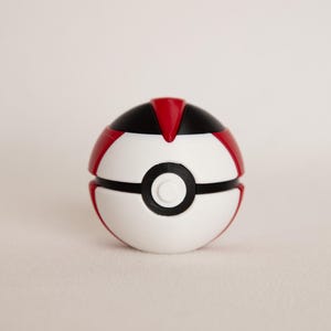 May include: A white and red Poké Ball with a black band and button. The top section is black with a red triangle. The ball is a sphere, and the design is symmetrical.