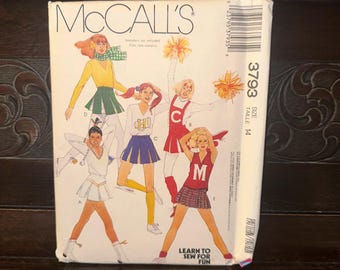 May include: A vintage McCall's sewing pattern featuring illustrations of cheerleaders in various outfits. The pattern includes images of cheerleaders in skirts, sweaters, and pom-poms. The text on the pattern reads "Learn to Sew for Fun."