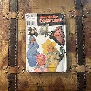 May include: A vintage Simplicity Costumes sewing pattern featuring illustrations of babies dressed as a bee, butterfly, and flower. The pattern is labeled 7868, size A, and is set against a brown trunk with a map design.