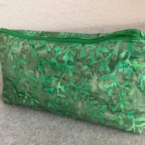 May include: A rectangular, green fabric pouch with a zipper closure. The pouch features a repeating pattern of leafy shapes in varying shades of green. The zipper and stitching are also green.