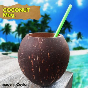 Può includere: Una tazza di cocco marrone con una cannuccia verde, sullo sfondo di una spiaggia tropicale. La tazza ha una superficie naturale e strutturata e il testo "COCONUT Mug." è visibile. Le parole "made in Ceylon" sono visibili.